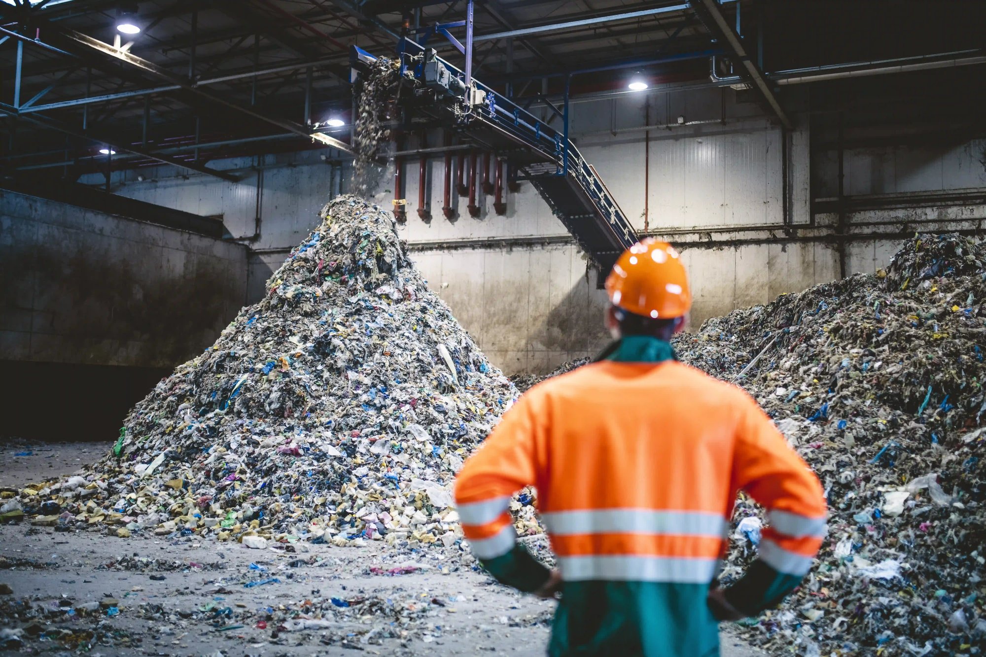 a person in orange hard hat standing in a large pile of garbage