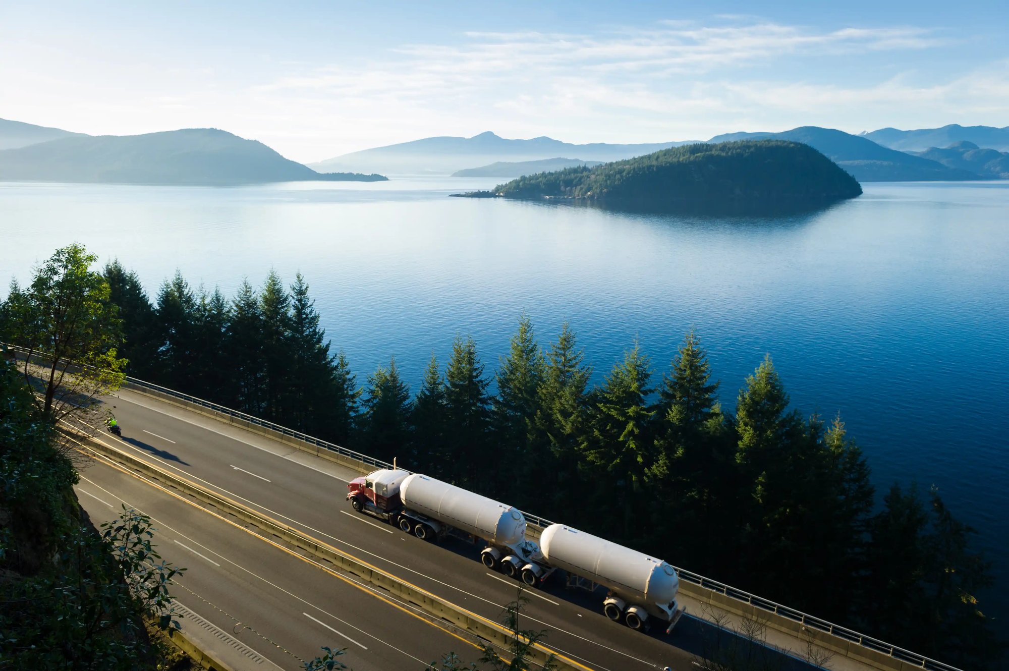 un camion sur la route avec un plan d'eau et des montagnes en arrière-plan