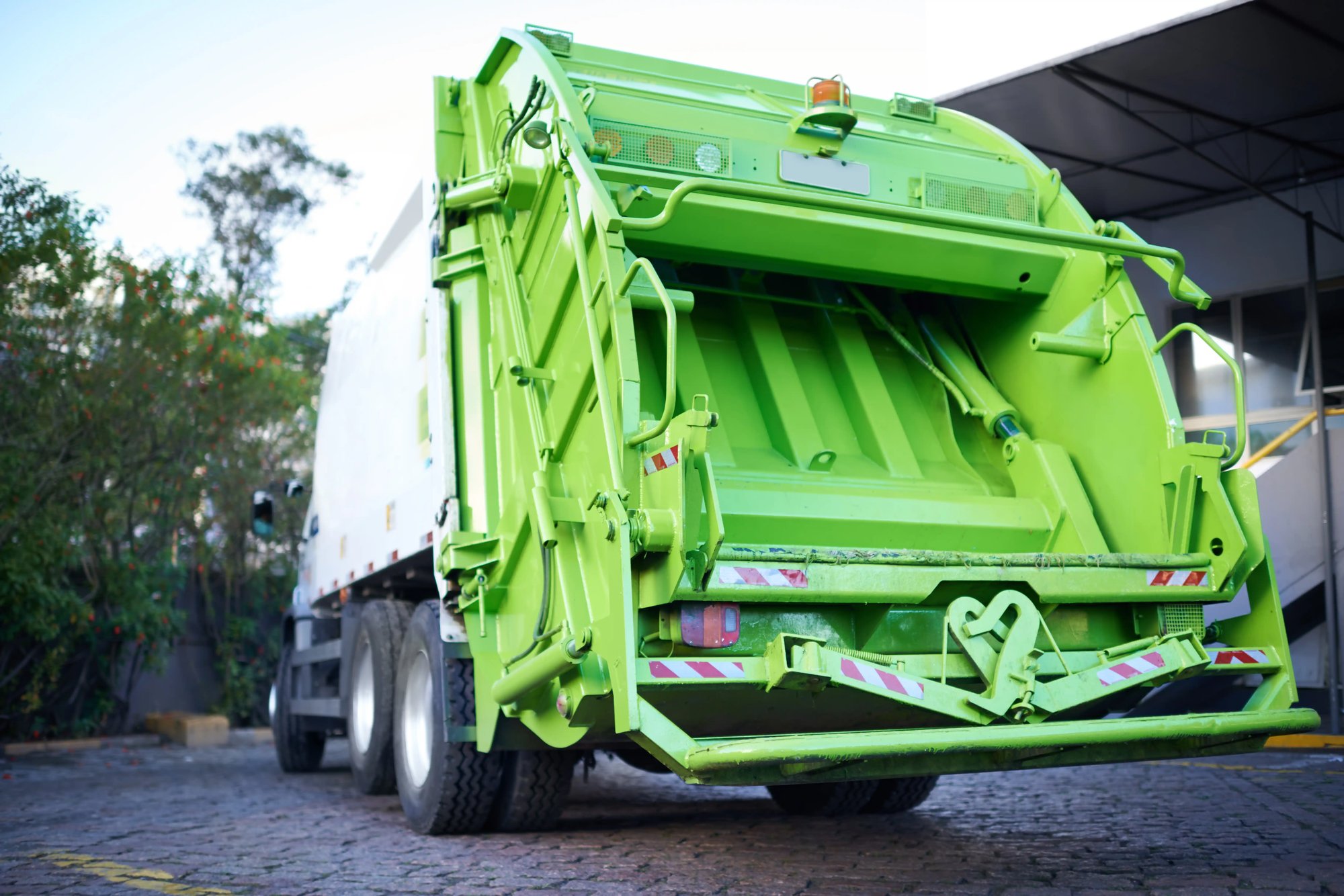 a green garbage truck parked on a brick road