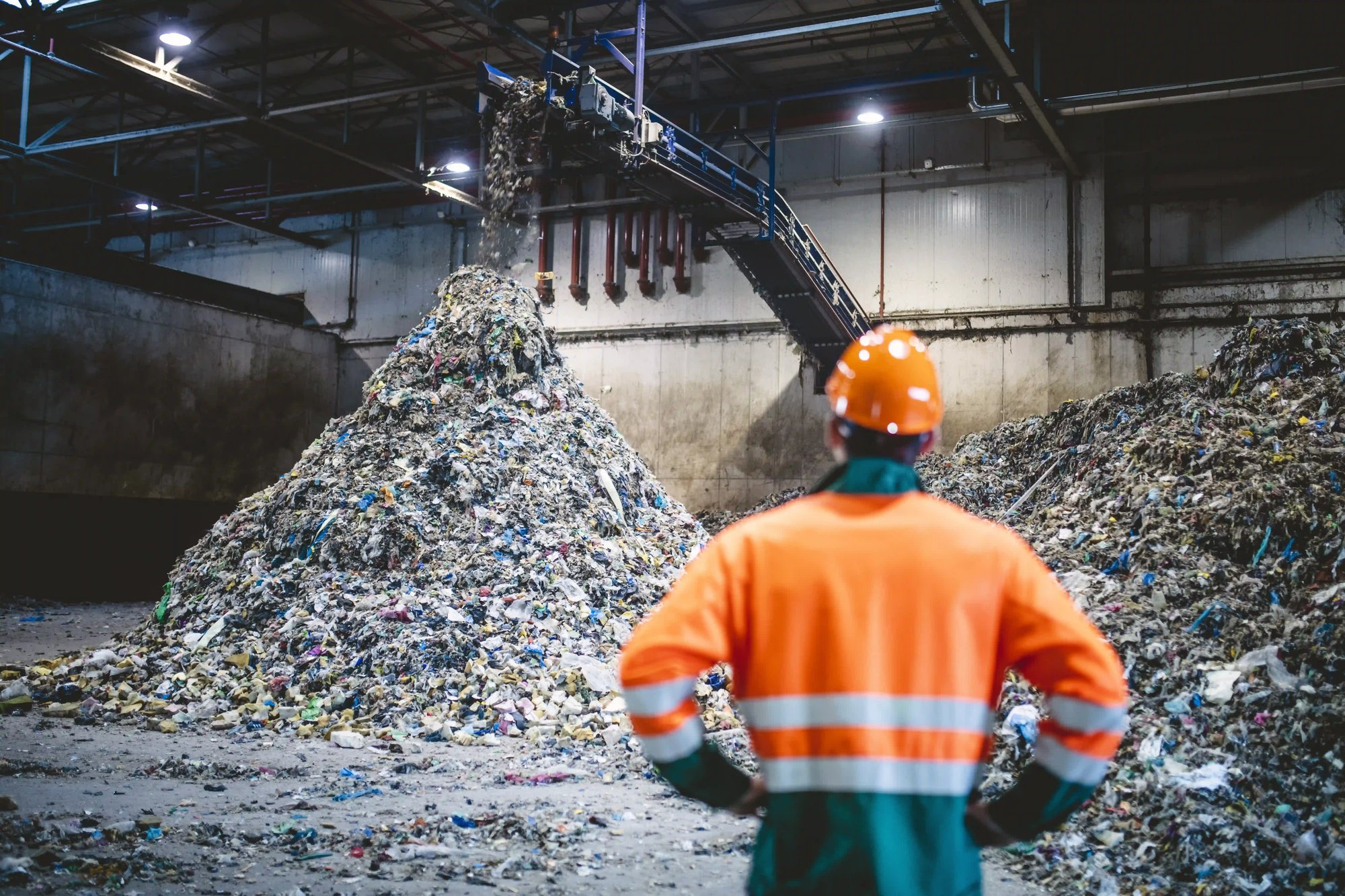 a person wearing an orange hard hat standing in front of a large pile of garbage